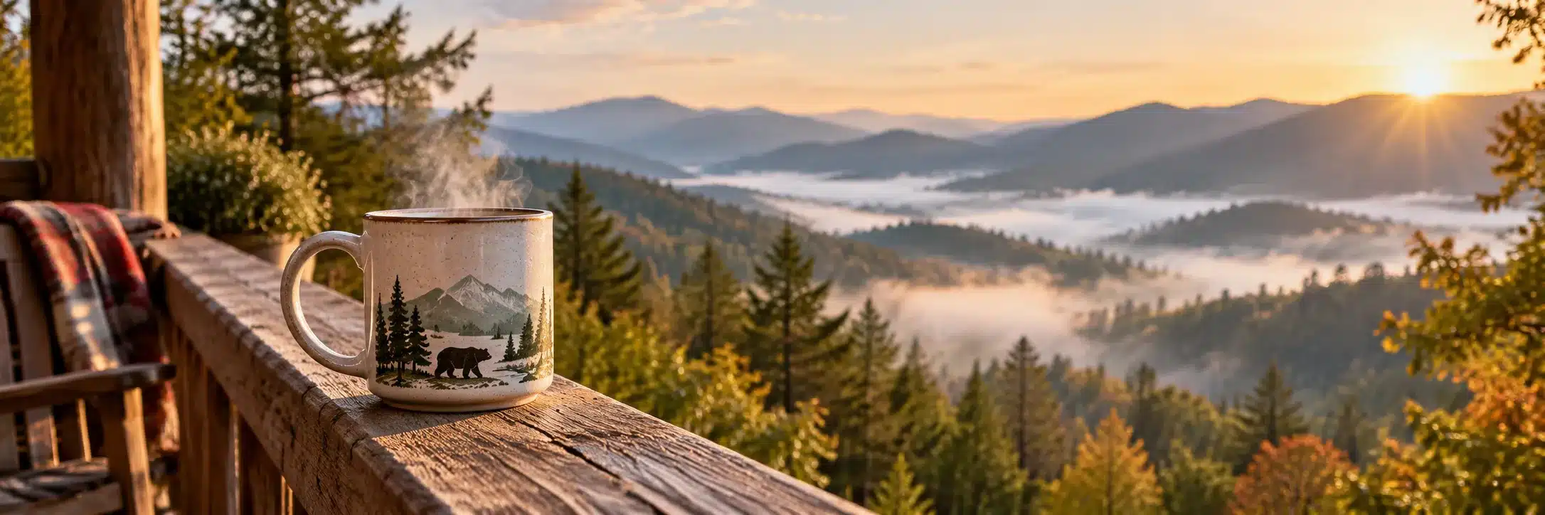 A camp mug with a bear design sitting on a cabin porch rail with Smoky Mountain ridges in morning haze behind it